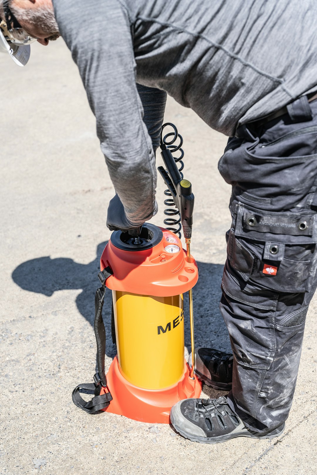Man Operating A Yellow And Orange Pressure Sprayer Outdoors K5bsrdqmc2q